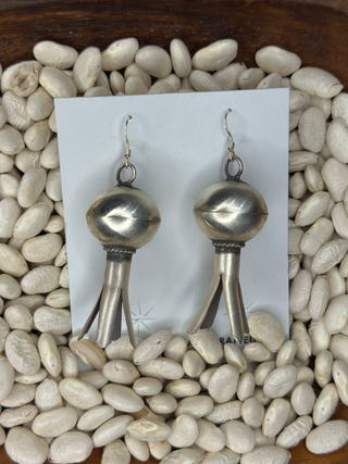Pair of silver earrings on a white card with pebbles in the background